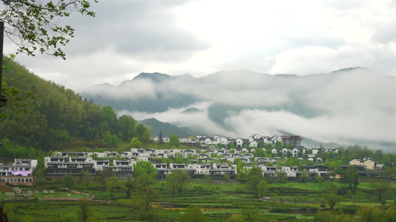 Aerial photography of high mountains shrouded in clouds and mist after rain, humid climate, and green forests shrouded in mist，Huizhou style architecture in southern Anhui, China
