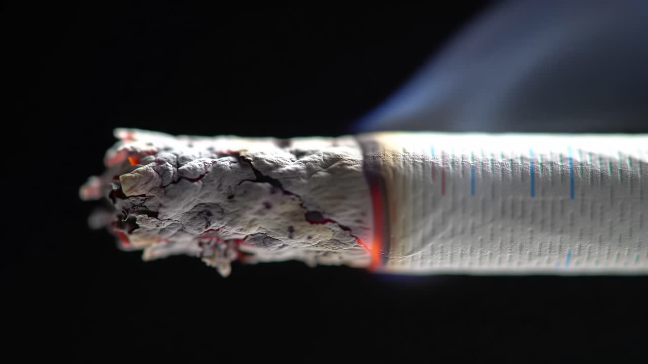 Close-Up Shots of a Burning Cigarette Featuring the Smoldering Ash and Smoke Emissions, Highlighting Its Intricate Details and Texture in Dark Settings