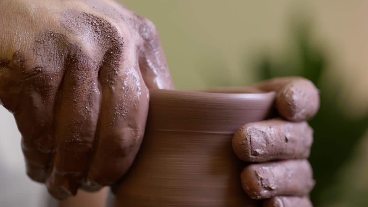 Male potter hands shaping raw clay vase neck close up on pottery turntable wheel