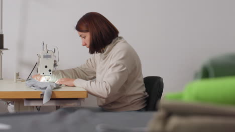 fashionista seated at machine, carefully sewing garment in bright workspace with calm posture and skillful control, shaping fabric into stylish creation for professional finishing success
