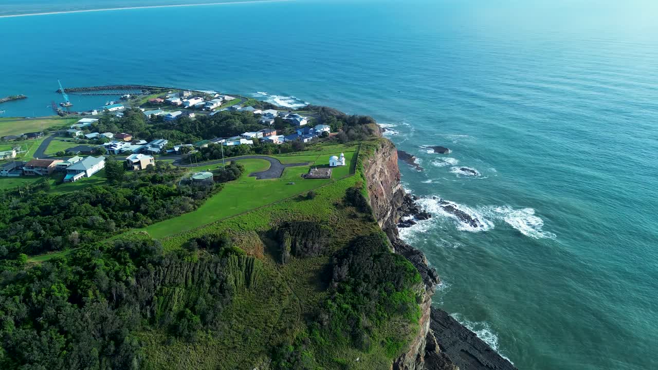 Drone aerial landscape of Crowdy Head lighthouse beacon tower building on top of bushland forest cliffs with suburban town housing along headland ocean coastline in Australia travel tourism outdoors