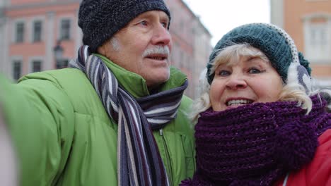 couple of senior tourists taking selfie in winter city center smiling, looking at camera, blog, vlog