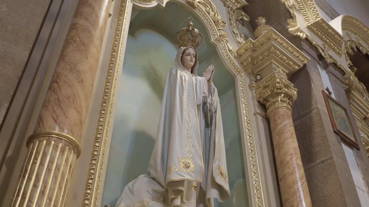 Interiér katolického kostela se sochou Panny Marie s korunou a bílým rouchem, umístěnou ve zdobeném oltářním výklenku, symbolizující oddanost, modlitbu a mariánskou víru.
