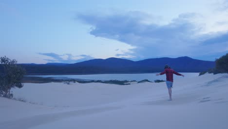 Toma-En-Cámara-Lenta-De-Un-Hombre-Caminando-Hacia-Hermosas-Dunas-De-Arena-Con-Vista-A-Un-Lago-En-Victoria-Australia