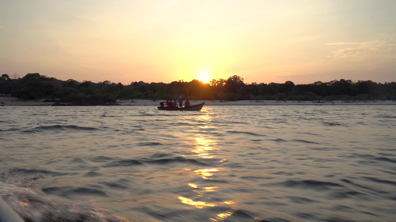 pequeño barco de pesca cruza otro barco en una puesta de sol en la selva amazónica