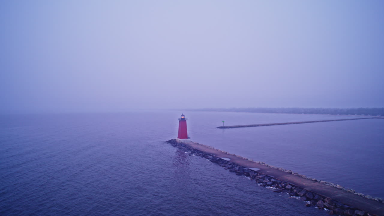 Foggy Drone shot flying backwards away from lighthouse on the end of a breakwater in lake michigan
