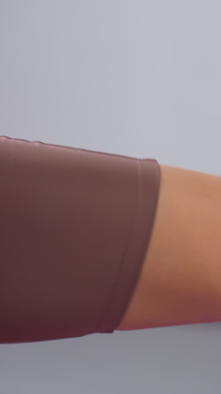 primer plano de una mujer con ropa deportiva marrón estirando la pierna en el gimnasio, pie con calcetín blanco, ligeramente elevado, fondo borroso con equipos de gimnasio y detalles de colores pastel visibles