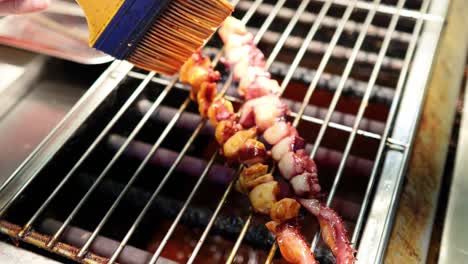 squid skewers being brushed with sauce on grill