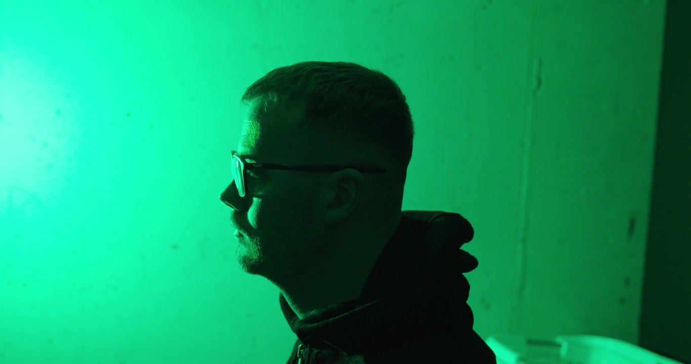 Silhouette di una persona incappucciata che indossa una felpa con cappuccio sotto un'illuminazione verde. Concetto drammatico di anonimato, segretezza, cybersecurity e mistero.