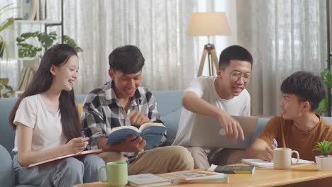 asian teen group studying at home. a boy holding a laptop discussing with his friends, writing into notebook. a boy in plaid shirt with a book teaching a girl and friends.