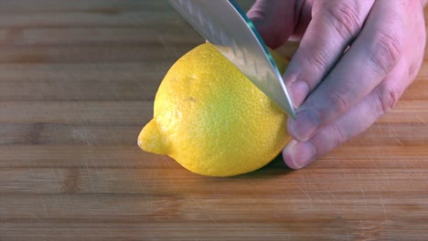 slicing a fresh lemon with a chefs knife on a wooden chopping board in the kitchen