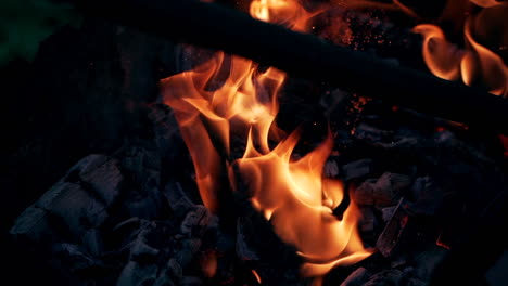 Explosion of flame with bright sparks. Black smoldered logs explode with fiery flame on dark background outdoors. Close-up.