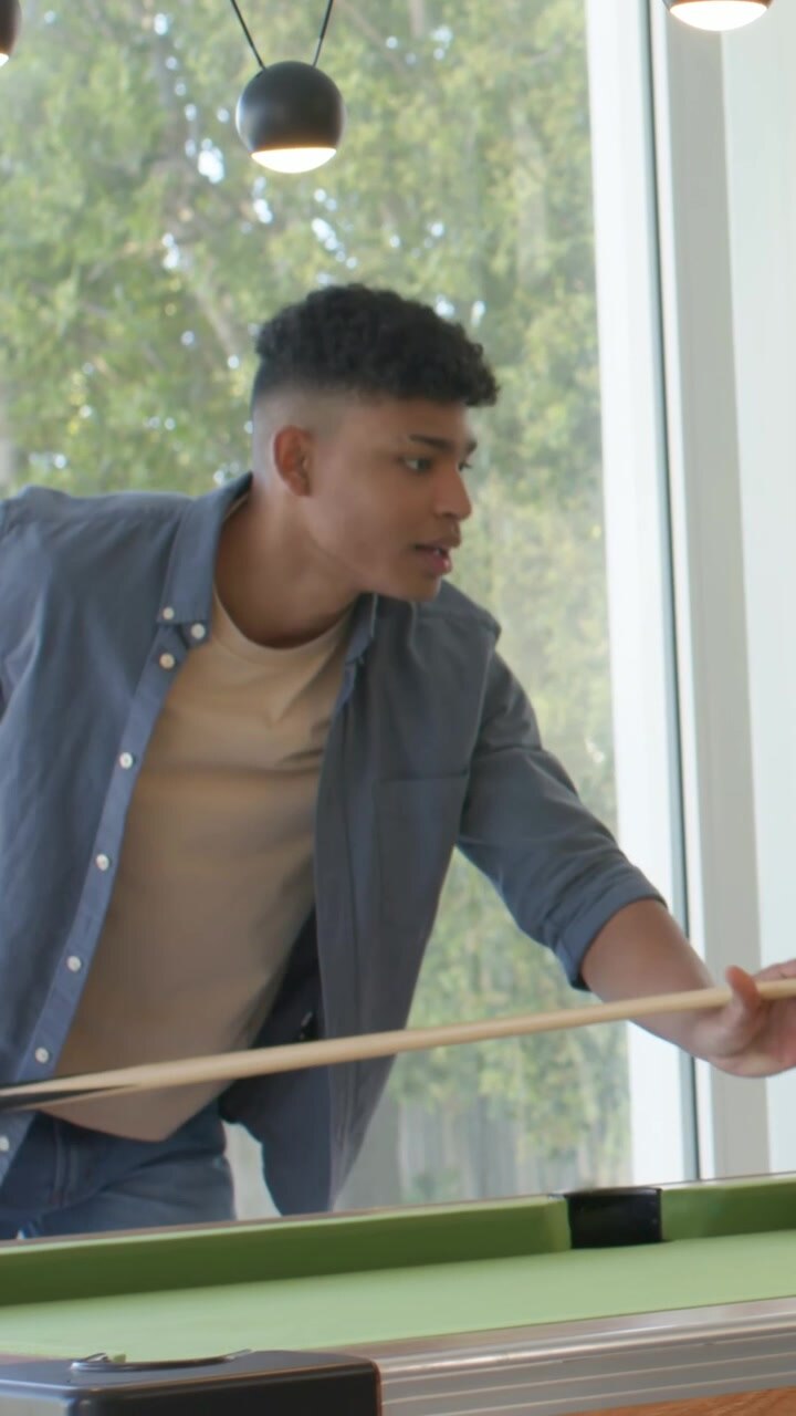 Vertical video: Lining up shot, adult male striking cue trying to sink red ball on home pool table