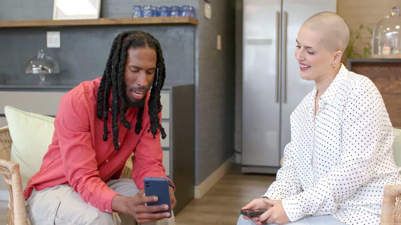 Diverse friends tapping and scrolling smartphones at coffee table, leaning in, sharing app finds