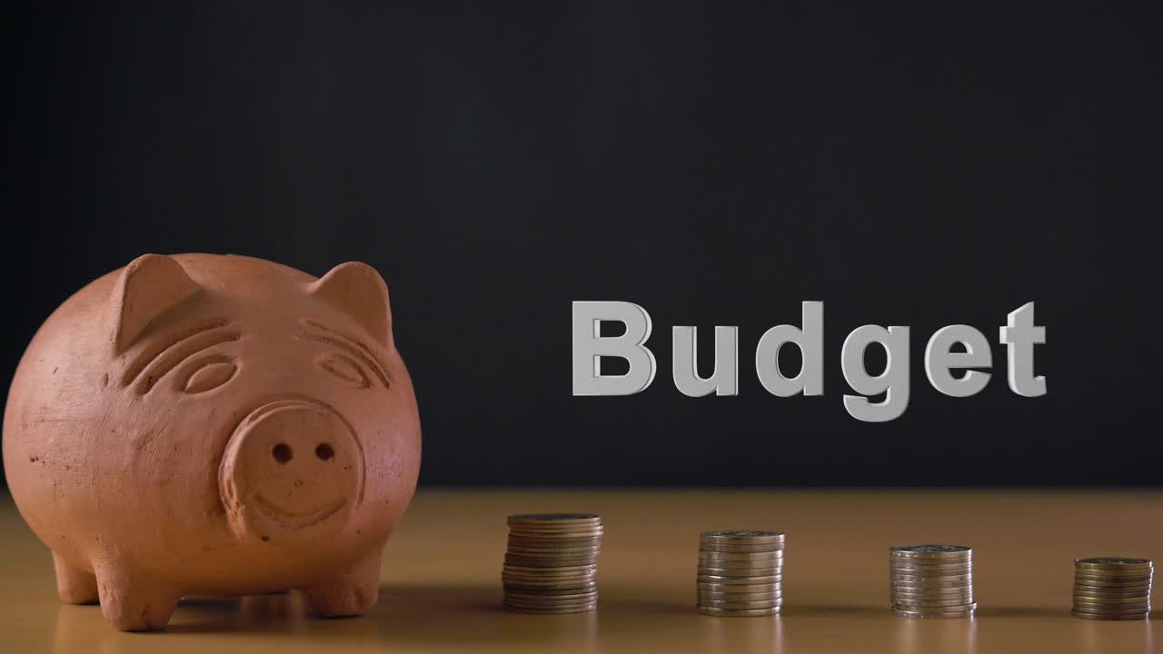 Teksten 'Budget' og en hvid mands hånd der lægger en mønt i en sparegris af ler