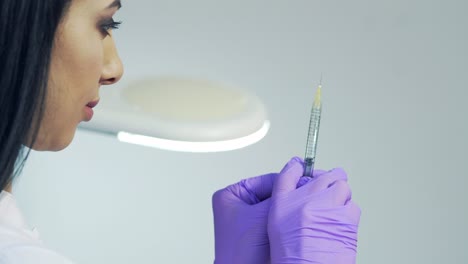 Hands of the beautician in purple gloves holding syringe. Cosmetologist prepares for a injection cosmetology procedure