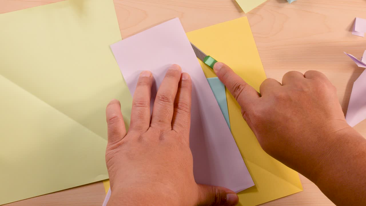 Person uses scissors to cut white paper for origami, overhead view, bright even lighting