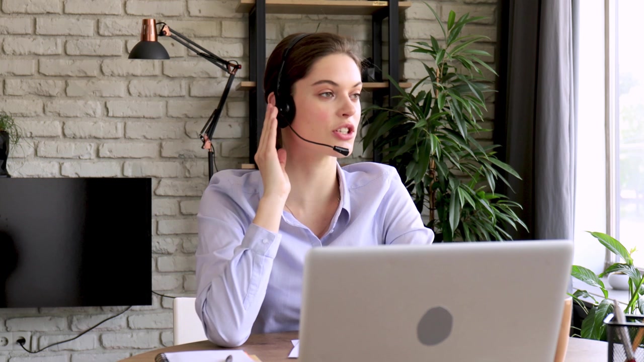 Giovane donna con cuffie che parla e lavora al laptop