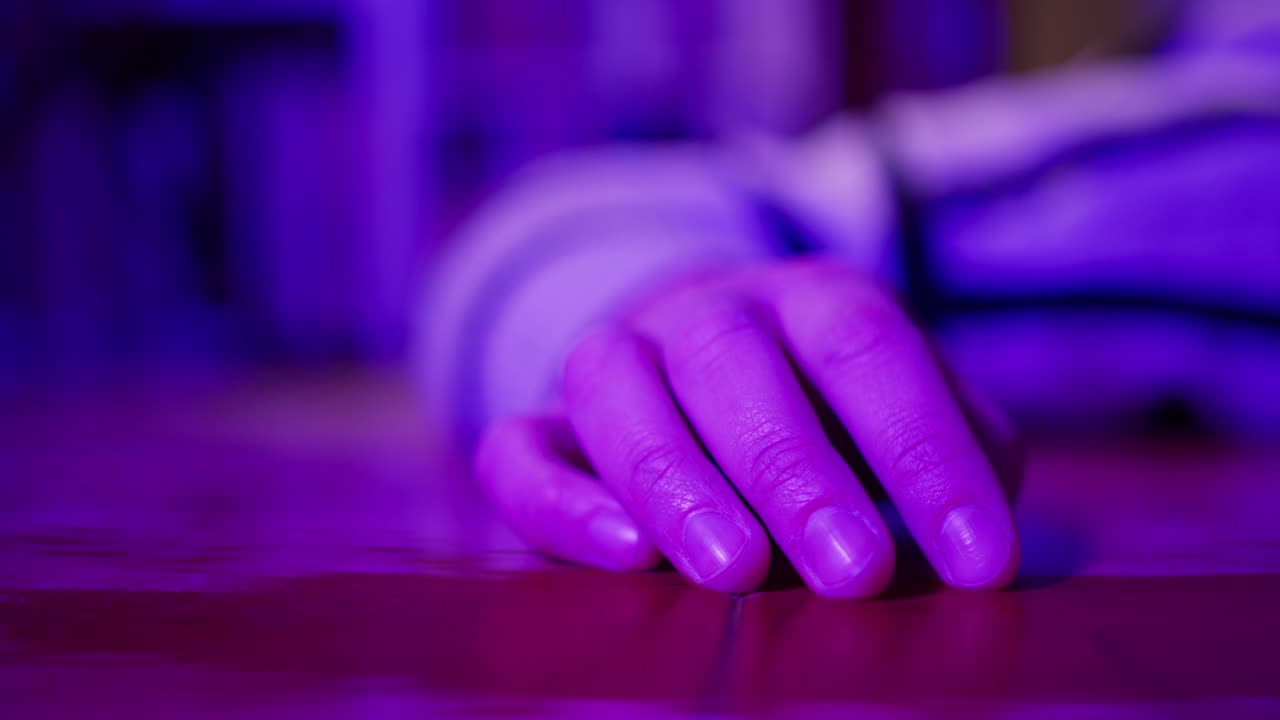 Primo piano di una mano umana appoggiata su un tavolo sotto una luce viola