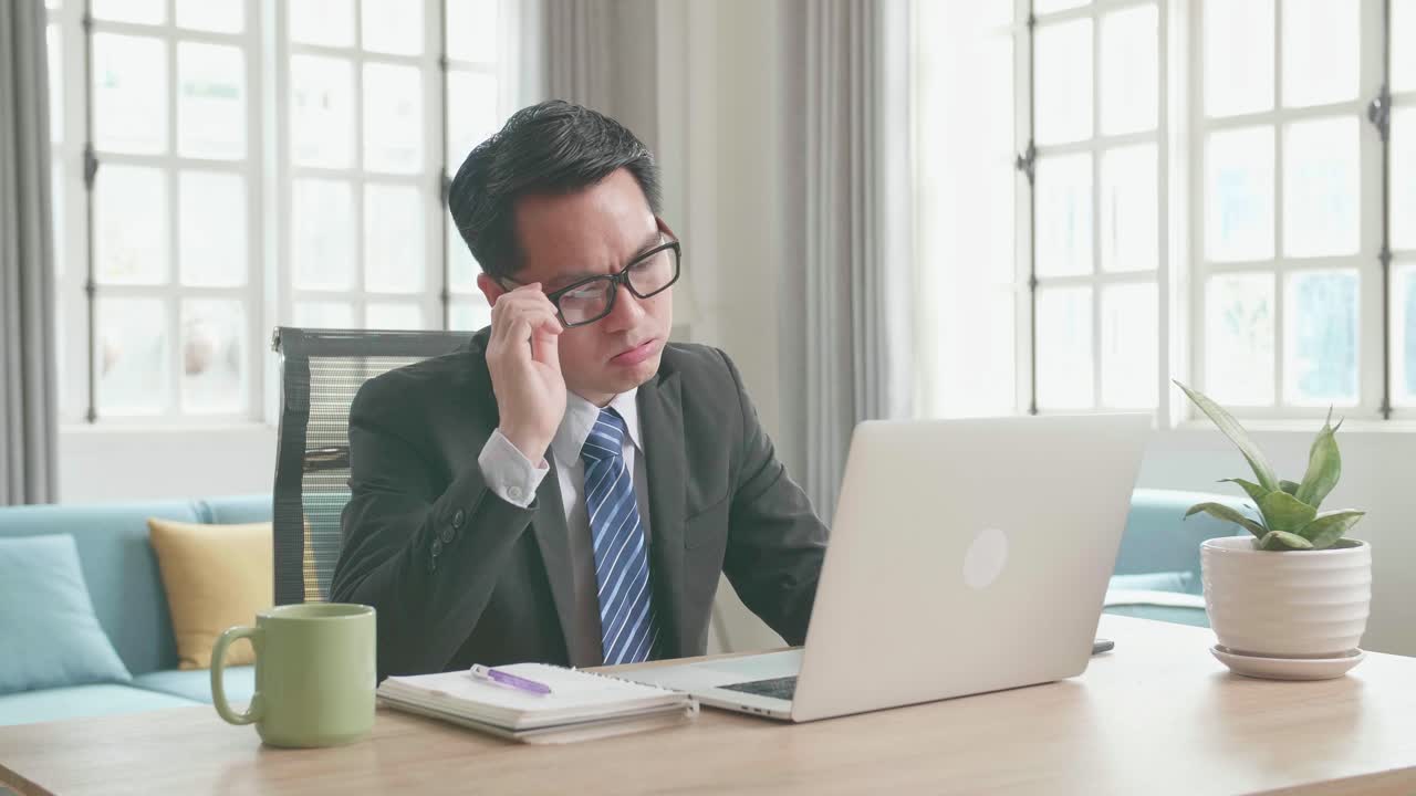 Tired Asian Businessman In Business Suit Taking Off The Glasses After While Using The Computer For Working At Home.