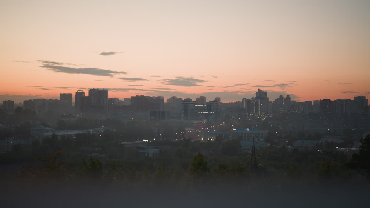 sunrise city skyline with morning mist soft orange sky over distant highrise silhouette, fog drifting across rooftop vegetation, scattered urban lights glowing, calm reflective atmosphere ideal