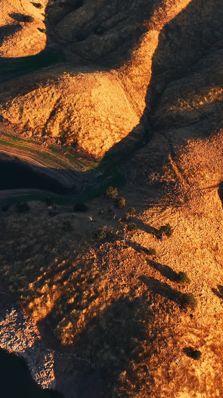 Flying above the rolled tops of mountains lit with setting sun. Panorama of rocks in California with lake at the foot. Bird's eye view. Vertical video