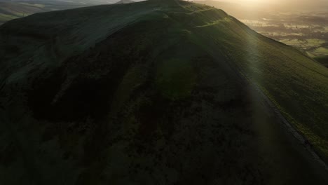 Dramatic-aerial-tilt-up-reveal-establishing-shot-of-people-stood-at-Mam-Tor-trig-point-enjoying-the-views-and-sunrise-with-lens-flares