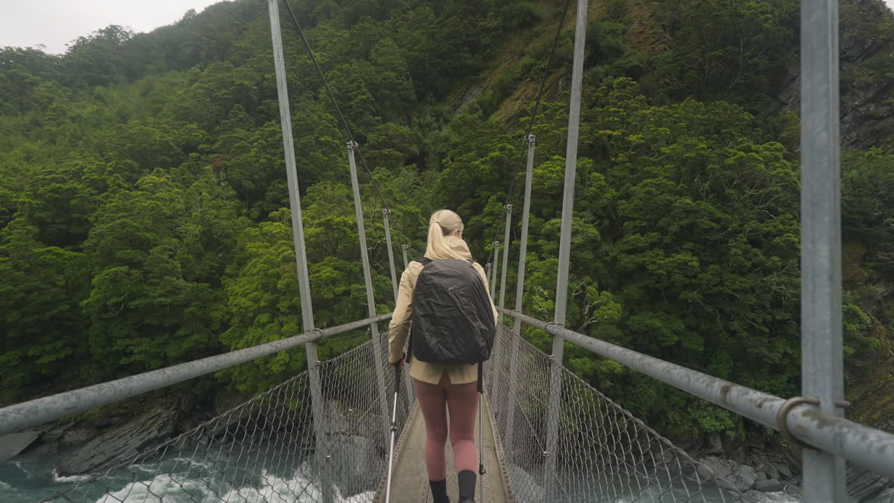 뉴질랜드의 자연 산책로에서 현수교를 건너는 여성 모험 백패커