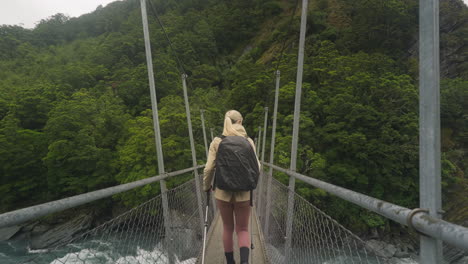 mochilero de aventura femenina cruzando el puente colgante durante el sendero natural en nueva zelanda