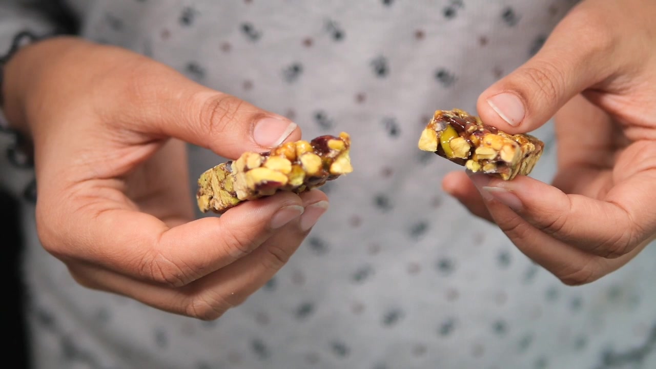 Persona che tiene in mano una barretta energetica spezzata a base di frutta e noci