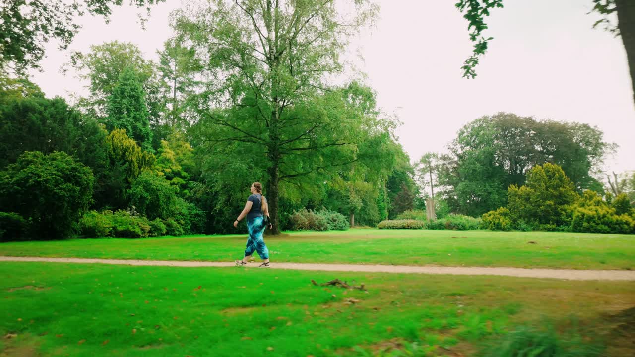 una hembra blanca caucásica con una mochila camina a través de un exuberante parque verde en un soleado día de verano, capturada desde un tiro de muñeca lateral