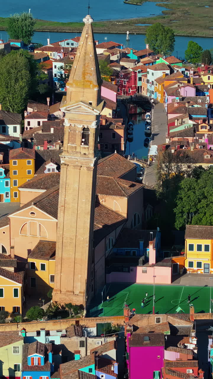 Aerial drone view of the Church of Saint Martin Bishop surrounded by colourful houses in Burano Island, Italy. Vertical