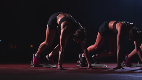 female runners at athletics track crouching at the starting blocks before a race. in slow motion.