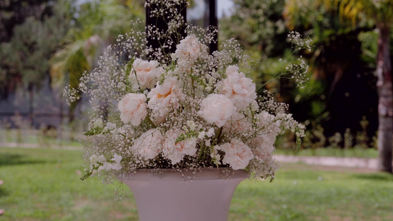 Elegant floral arrangement featuring white flowers and baby's breath in a decorative vase, enhancing an outdoor wedding celebration