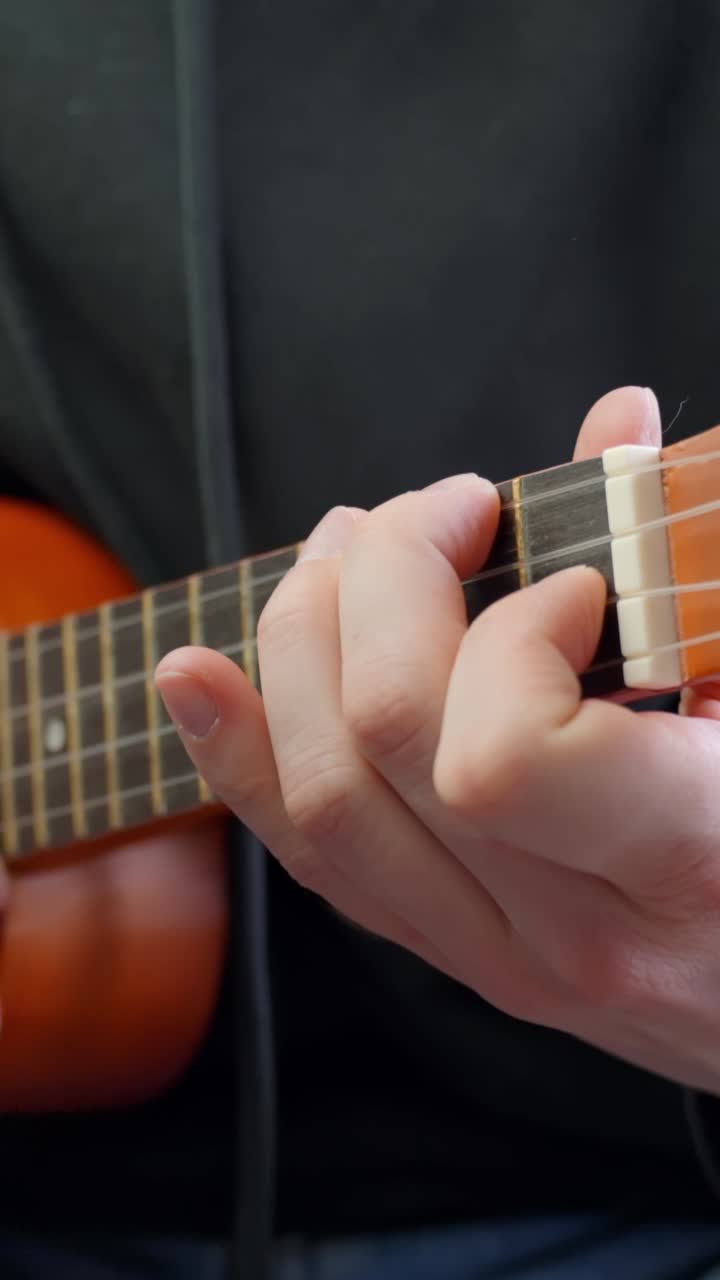 Mid shot of fingers picking melody on acoustic ukulele while relaxed at home