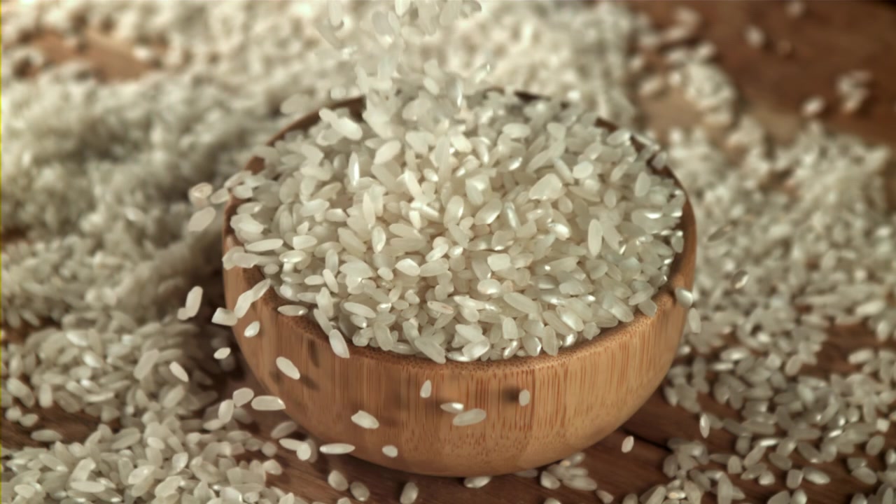 Hvide ris falder ned i en træskål i slowmotion