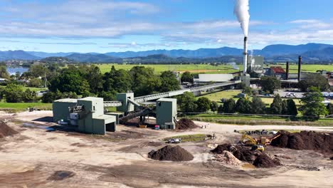 aerial footage of a sugar mill with smoke stacks, surrounded by lush greenery and mountains under clear skies