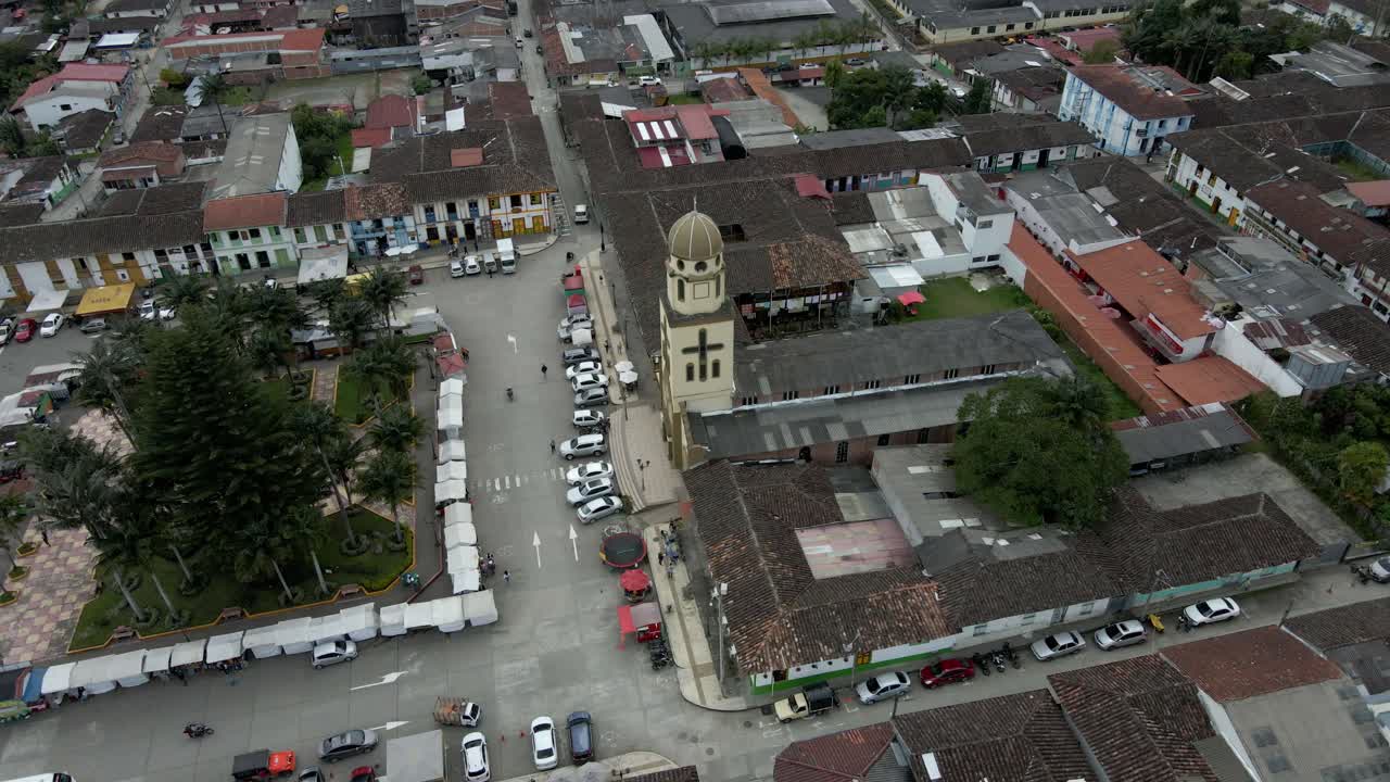 A tranquil aerial orbit of Salento church plaza with cars parked and bustling market stalls