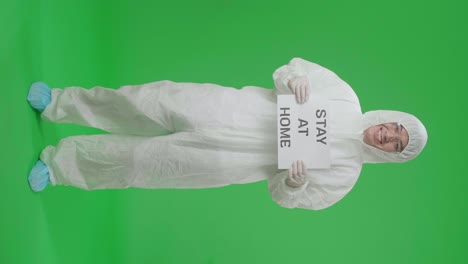 full body of asian man wearing personal protective equipment uniform ppe and holding stay at home sign in the green screen studio