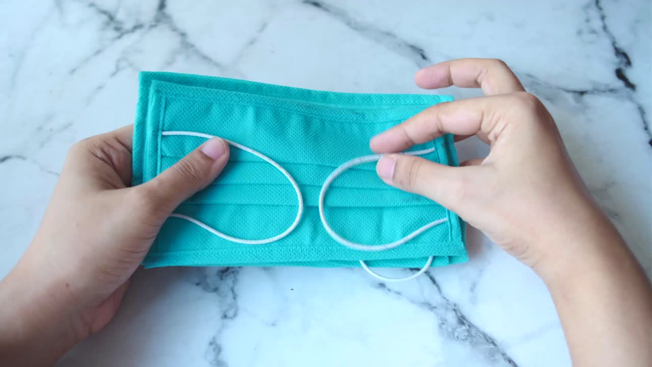 manos sosteniendo una máscara facial azul azul desdoblada