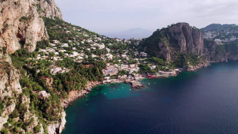 A-wide-aerial-shot-of-the-beautiful-beaches-and-rocky-cliff-landscape-around-Marina-Piccola-on-Capri,-a-famous-island-that-is-a-popular-luxury-vacation-destination-in-Italy-along-the-Amalfi-Coast