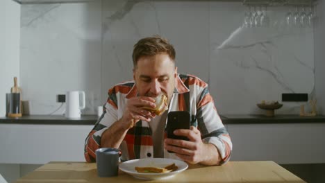 man eating sandwich and using smartphone