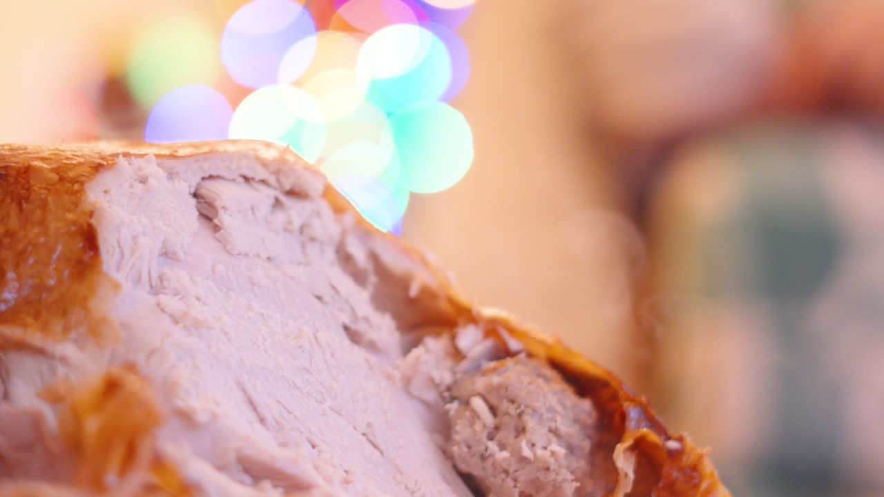 한 피부를 가진 전통적인 칠면조는 가족 구성원이 손님에게 음식을 제공 할 때 배경에 크리스마스 조명과 함께 저녁 식사 테이블에서 조각됩니다.