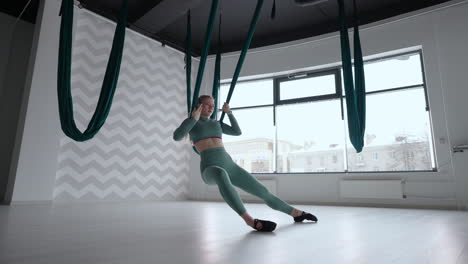 young smiling woman practice in aero stretching swing. aerial flying yoga exercises practice in green hammock in fitness club