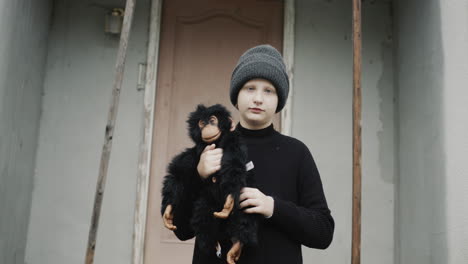 Portrait-of-a-sad-girl,-standing-on-the-threshold-of-the-house,-holding-a-toy-monkey-in-her-hands