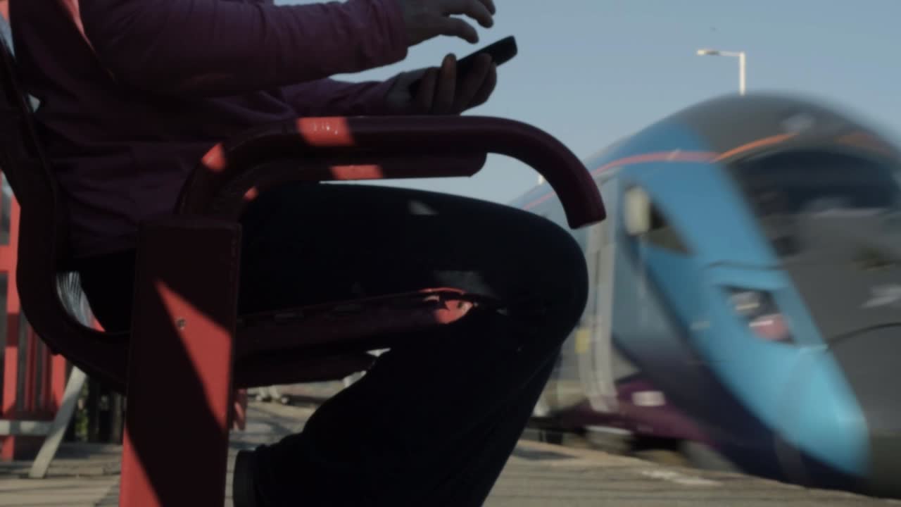 Hands using a mobile phone on train platform as train speeds by medium shot