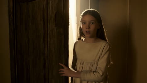 scared young girl peeking from behind a dark door