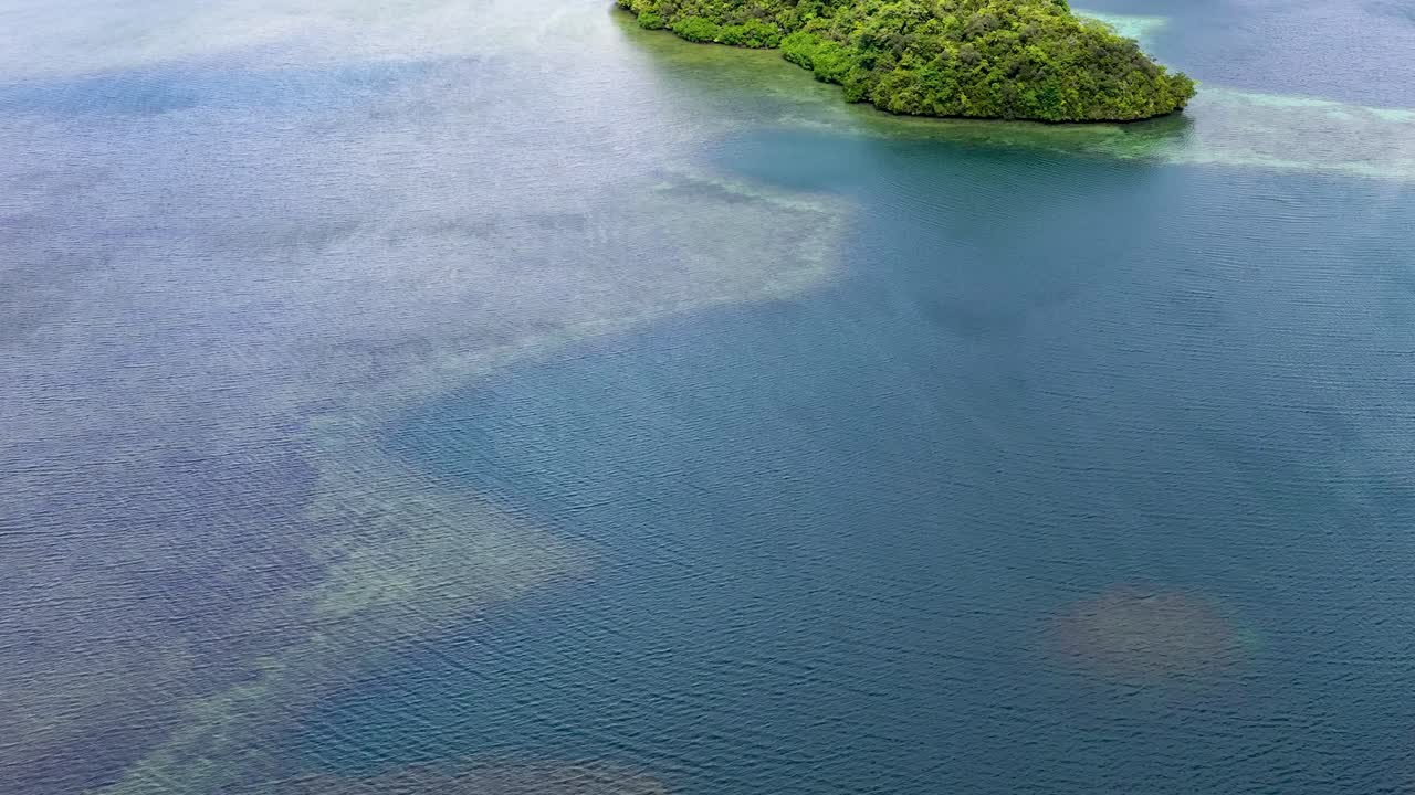 Droneopptak fra høy vinkel som glir over turkist havvann og frodige, grønne kalksteinsøyer