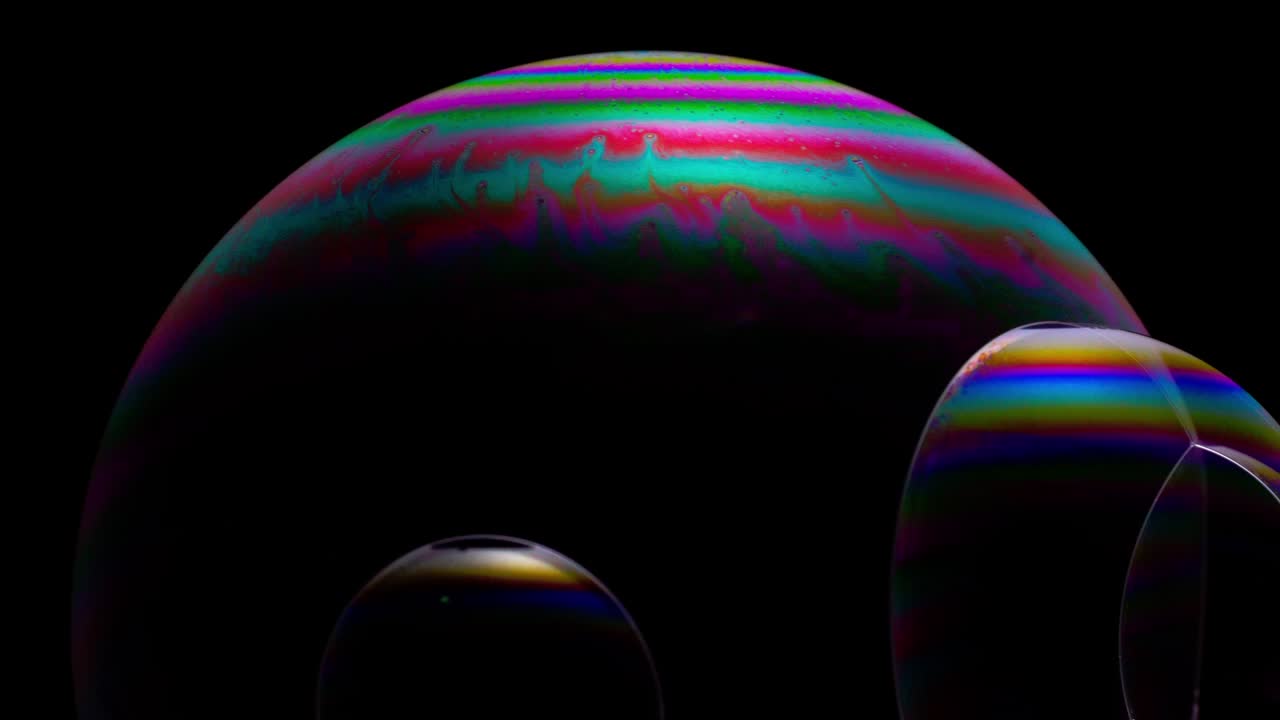 Close-up of soap bubbles on a dark background, with a vibrant, multicolored, iridescent surface, resembling a science fiction landscape