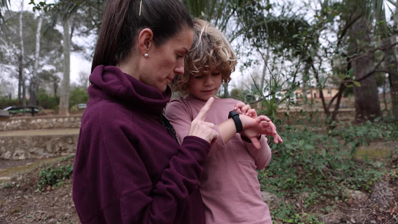 mamá explicando a su hijo cómo usar un reloj de pulsera al aire libre